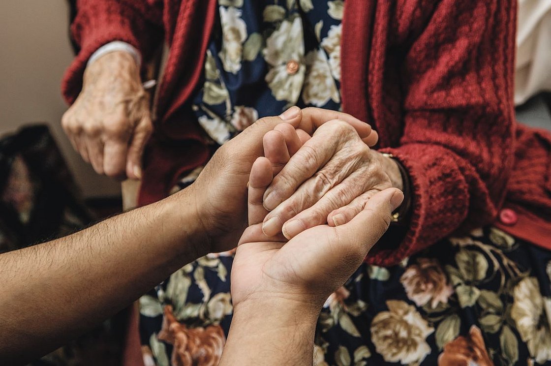 Eine jüngere Person hält die Hand einer älteren Frau