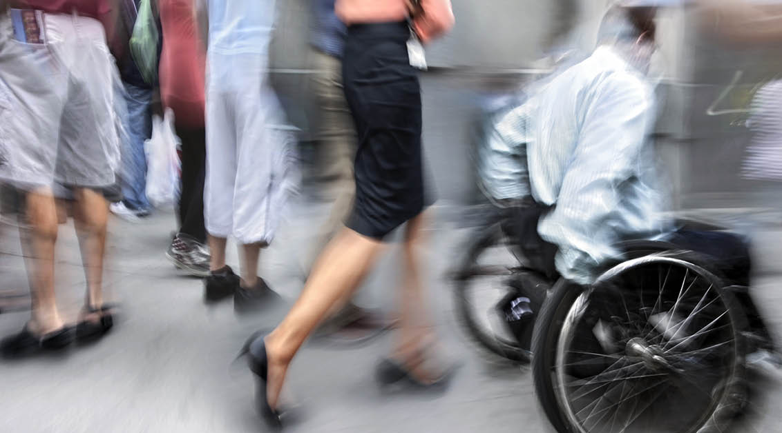 Verschwommenes Bild von Menschen auf der Straße. Unter ihnen ein Rollstuhlfahrer.